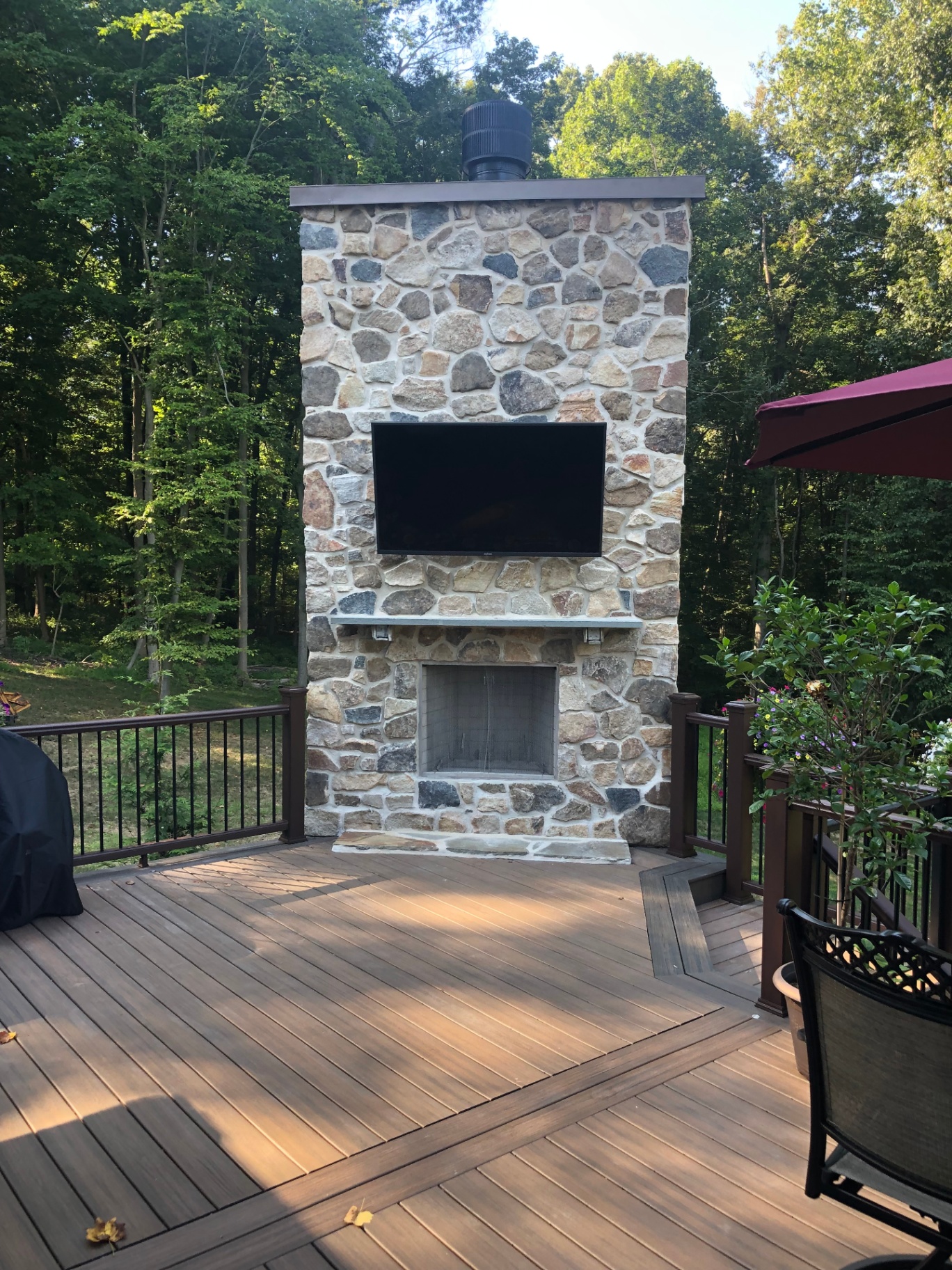 Stone fireplace with mounted outdoor TV on composite deck